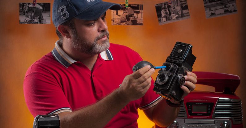 Lubrication - Concentrated male worker in cap applying oil to vintage film camera while sitting at table with assorted lubricant tubes and photo cameras