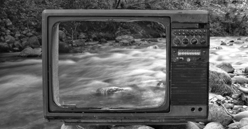 Water Damage - Black and white vintage old broken TV placed on stones near wild river flowing through forest